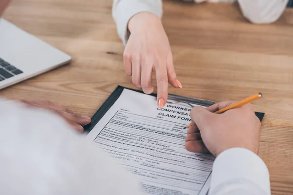 Cropped view of businessman filling in compensation claim form at workplace, compensation concept — Stock Photo