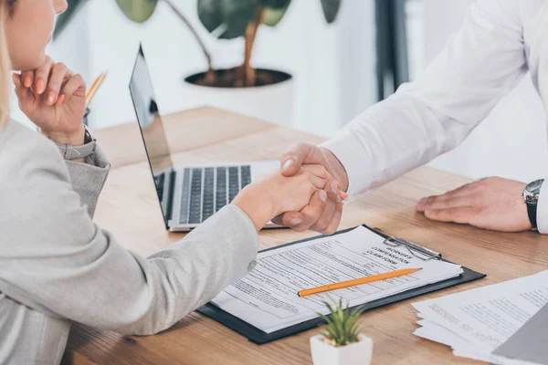 Cropped view of businessman shaking hands with woman at workplace, compensation concept — Stock Photo