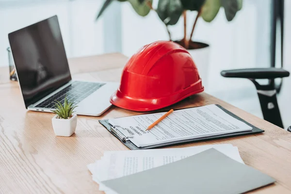 Portapapeles con formulario de reclamación de compensación y casco rojo en el escritorio de la oficina - foto de stock