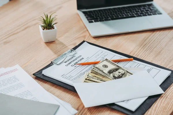 Clipboard with compensation claim form and open envelope with money lying over on office desk, compensation concept — Stock Photo