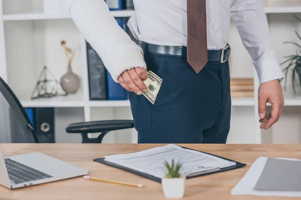 Vista recortada del trabajador con el brazo roto sacando dinero del bolsillo y de pie en la mesa en la oficina, concepto de compensación - foto de stock