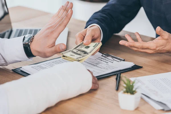 Cropped view of worker rejecting money giving businessman in blue jacket at table in office, compensation concept — Stock Photo