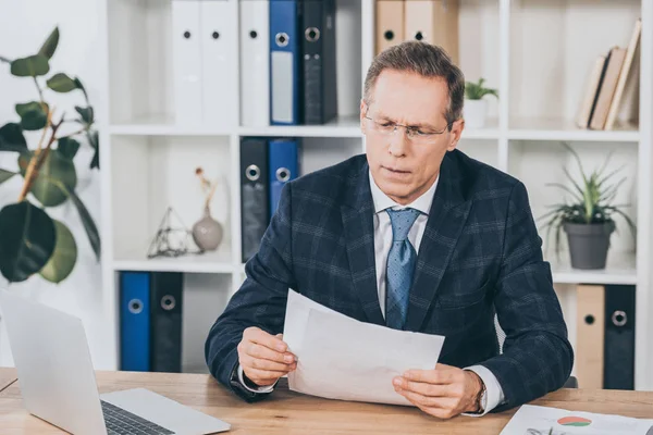 Uomo d'affari in giacca blu seduto a tavola e documenti di lettura in ufficio, concetto di risarcimento — Foto stock