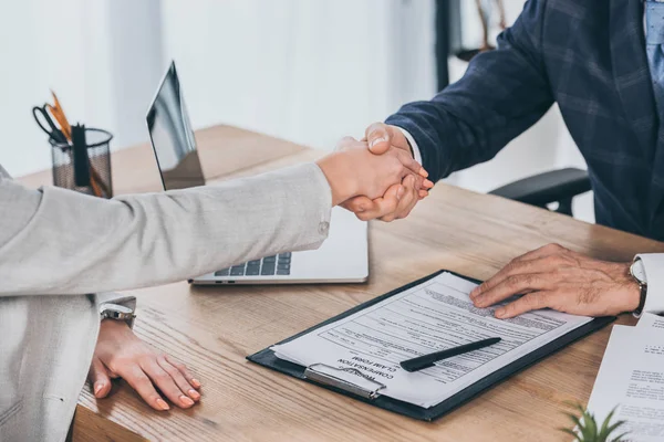 Cropped view of shaking hands businessman and woman over table in office, compensation concept — Stock Photo