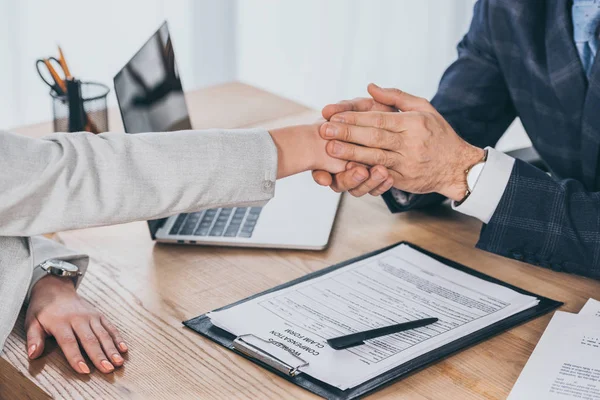 Cropped view of businessman holding woman hand over table in office, compensation concept — Stock Photo