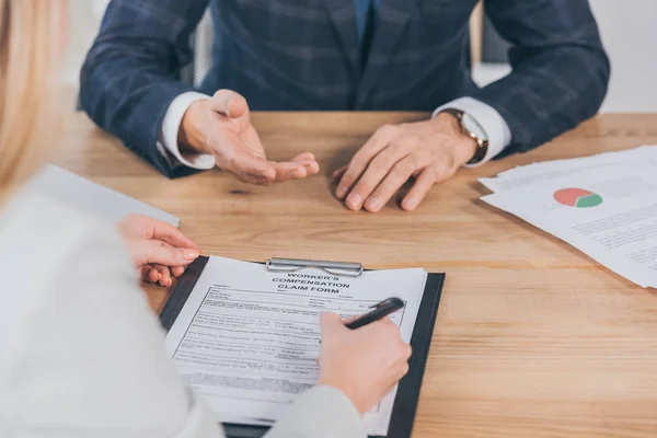 Abgeschnittene Ansicht einer Frau, die ein Formular für Schadensersatzansprüche unterschreibt und dem Geschäftsmann im Büro gegenübersitzt, Vergütungskonzept — Stockfoto