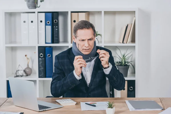 Businessman in neck brace sitting at table wiht documents, puting on glasses in office, compensation concept — Stock Photo