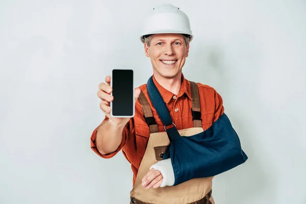 Repairman with arm bandage showing smartphone at white background — Stock Photo