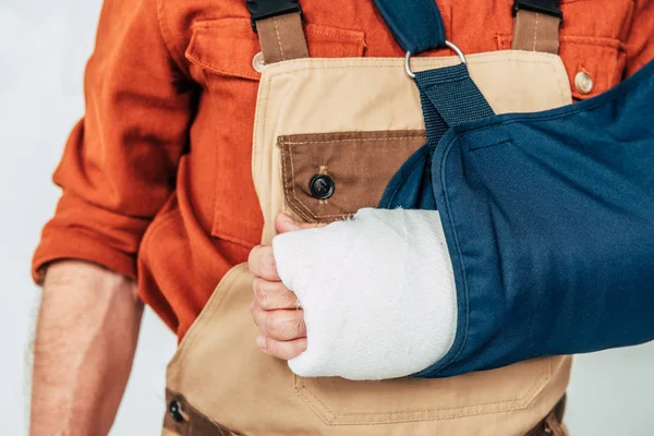 Vue recadrée du réparateur avec bras cassé et bandage sur fond blanc — Photo de stock