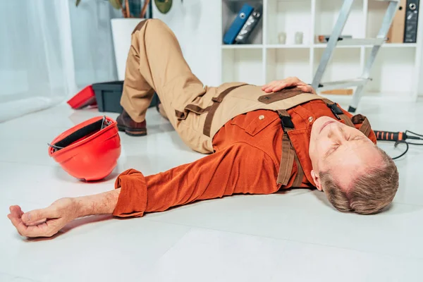 Reparador acostado en el suelo blanco en uniforme cerca de la escalera en la oficina - foto de stock