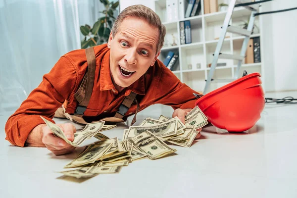Surprised repairman in uniform lying on floor near money in office — Stock Photo