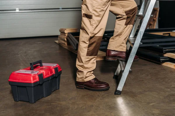 Cropped view of repairman in orange uniform climbing on ladder in garage — Stock Photo