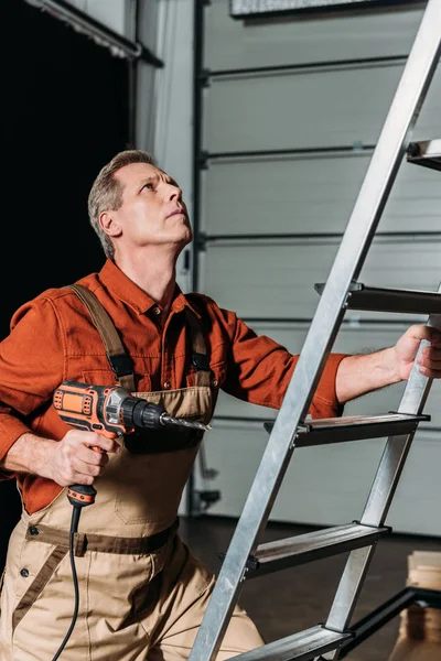 Reparador en uniforme naranja subiendo con destornillador en escalera en garaje - foto de stock