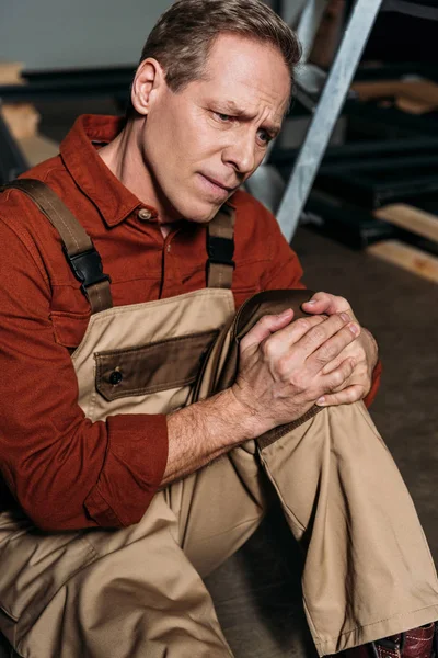 Repairman sitting on floor and holding injured knee in garage — Stock Photo