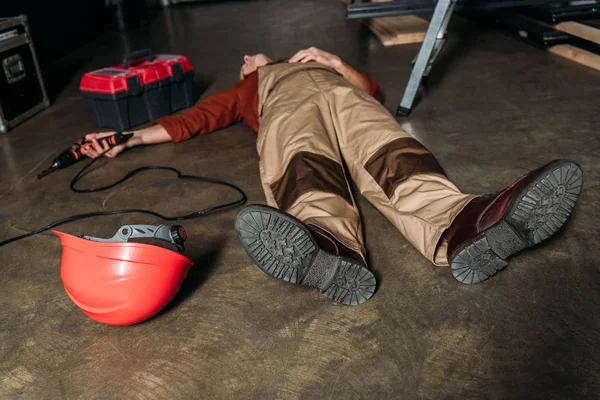 Réparateur couché sur le sol en uniforme près de l'échelle et tenant tournevis dans le garage — Photo de stock