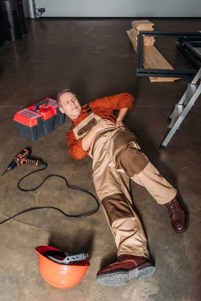 Reparador tumbado en el suelo cerca de la escalera y la celebración de lado en el garaje - foto de stock