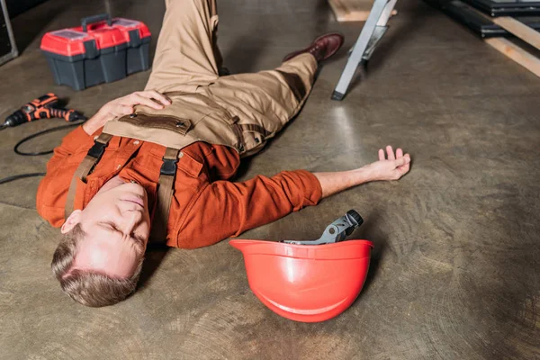Reparador de mediana edad acostado en el suelo cerca de escalera y hardhat en el garaje - foto de stock