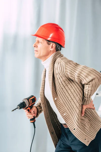Middle aged man in beige cardigan holding screwdriver and touching back at home — Stock Photo