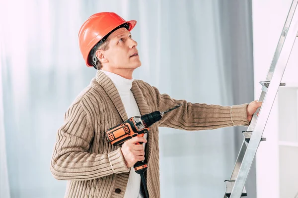 Homem em cardigan bege escalando com chave de fenda na escada em casa — Fotografia de Stock
