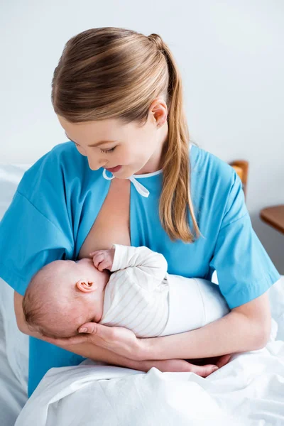 Feliz madre joven amamantando bebé recién nacido en la habitación del hospital - foto de stock