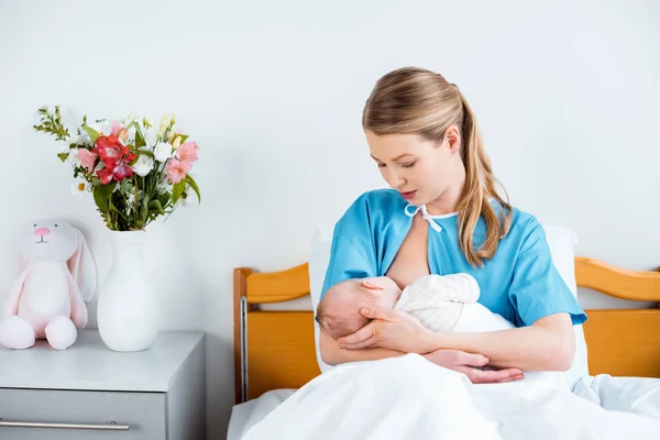 Junge Mutter sitzt im Bett und stillt Neugeborenes im Krankenhauszimmer — Stockfoto