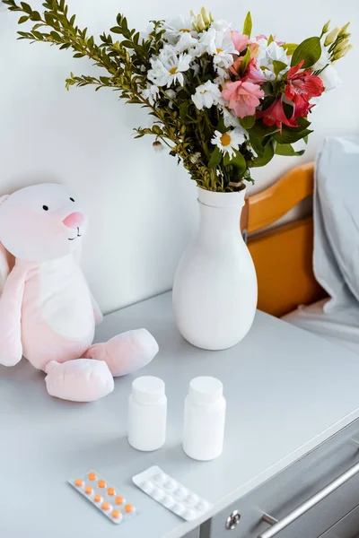 Primer plano vista de jarrón con flores, contenedores con pastillas y juguete en la mesa en el hospital - foto de stock