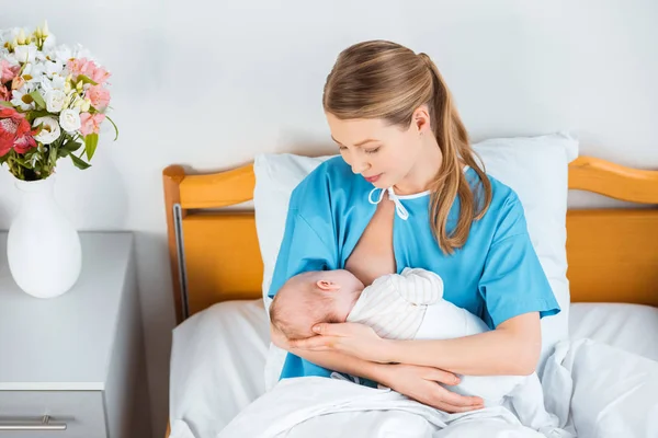 Blick aus der Vogelperspektive auf eine glückliche junge Mutter, die ihr Neugeborenes auf dem Bett im Krankenhauszimmer stillt — Stockfoto