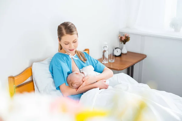 High angle view of happy young mother breastfeeding newborn baby on bed in hospital room — Stock Photo