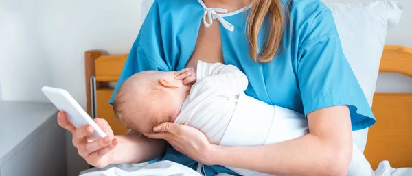 Cropped shot of mother breastfeeding baby and using smartphone in hospital room — Stock Photo