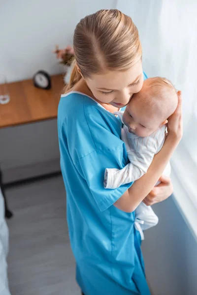 Hochwinkelaufnahme der schönen glücklichen jungen Mutter mit geschlossenen Augen, die ihr entzückendes Baby im Krankenhauszimmer umarmt — Stockfoto