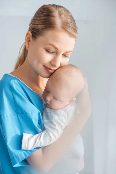 Bela feliz jovem mãe com olhos fechados abraçando adorável bebê no quarto do hospital — Fotografia de Stock