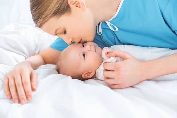 Jeune mère embrasser adorable nouveau-né couché sur le lit dans la chambre d'hôpital — Photo de stock