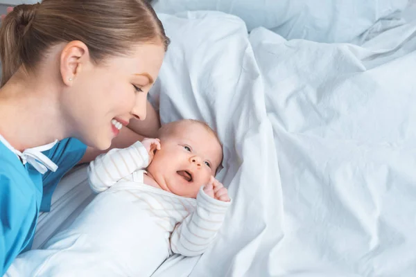 Blick aus der Vogelperspektive auf eine glückliche junge Mutter, die ihr entzückendes Baby auf dem Bett liegend betrachtet — Stockfoto
