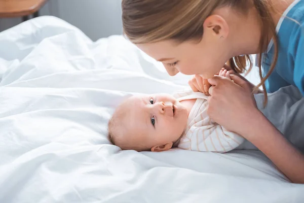 Vista lateral de la feliz madre joven cogida de la mano del adorable bebé en el hospital - foto de stock