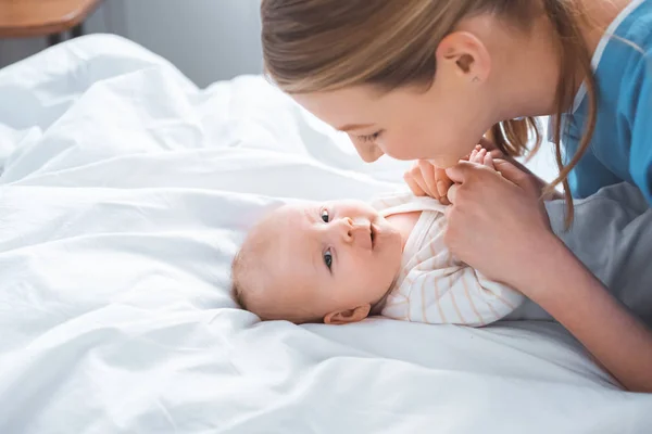 Vue latérale de heureuse jeune mère tenant la main d'adorable bébé à l'hôpital — Photo de stock