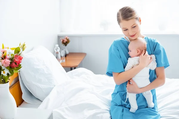 Blick von oben auf eine glückliche junge Mutter, die auf dem Bett sitzt und ihr Baby im Krankenhauszimmer hält — Stockfoto