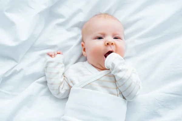 Vue de dessus de bébé adorable couché sur la literie blanche — Photo de stock