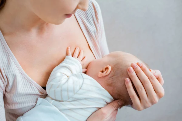 Cropped shot of young woman breastfeeding baby on grey — Stock Photo