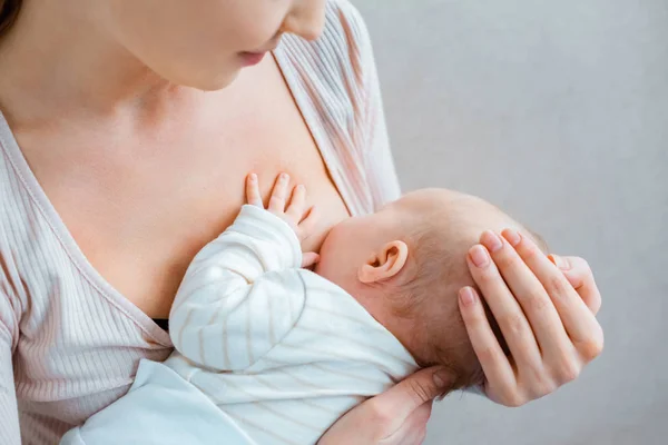 Colpo ritagliato di giovane donna che allatta bambino su grigio — Foto stock