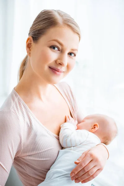 Hermosa madre joven amamantando bebé y sonriendo a la cámara - foto de stock