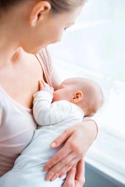 Tiro recortado de madre joven amamantando bebé adorable en casa - foto de stock