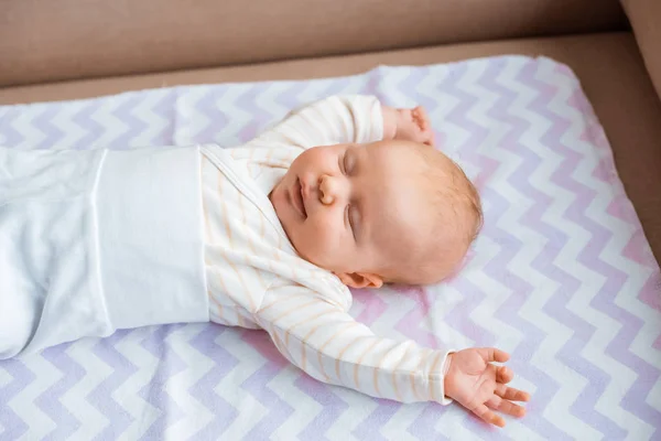 Adorable newborn baby with closed eyes and raised hands lying on sofa — Stock Photo