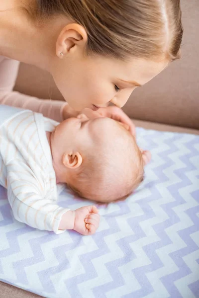 Glückliche junge Mutter küsst entzückendes Kind, das auf der Couch liegt — Stockfoto