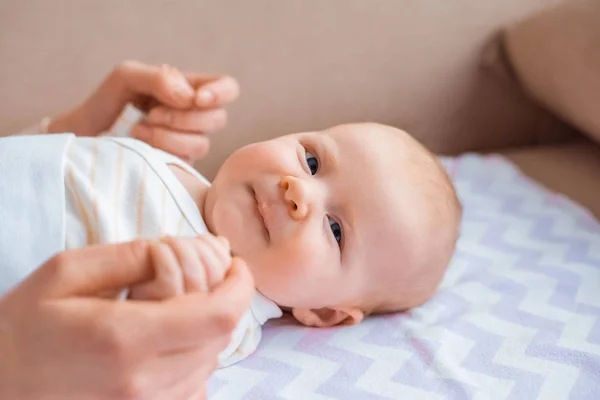 Cropped shot of mothe holding hands of adorable baby lying on couch and looking at camera — Stock Photo
