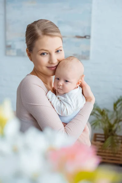 Messa a fuoco selettiva di felice giovane madre che abbraccia bambino e sorride alla macchina fotografica — Foto stock