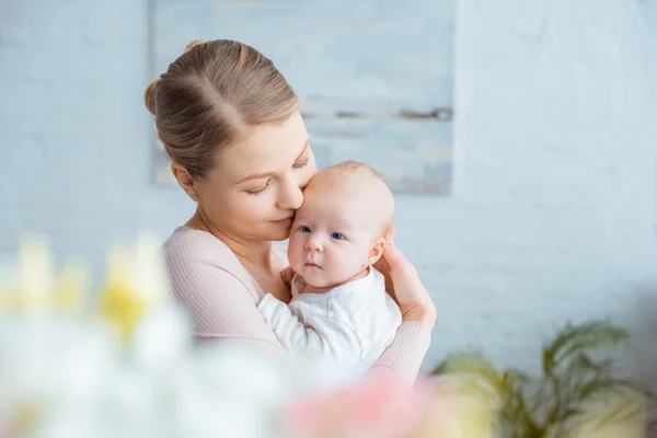 Selektiver Fokus einer glücklichen jungen Mutter, die ihr entzückendes Baby zu Hause umarmt — Stockfoto