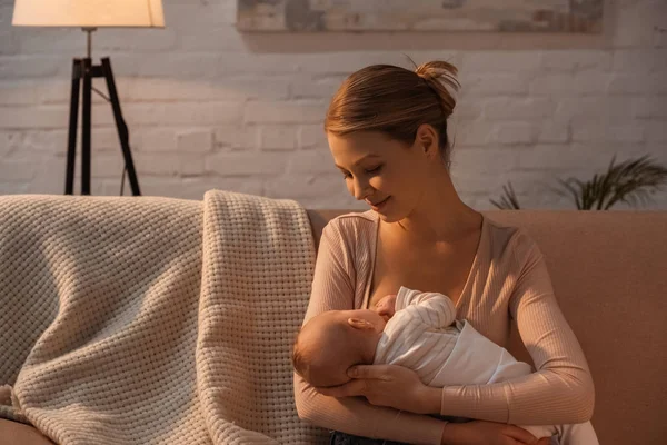 Smiling young mother breastfeeding baby at night — Stock Photo