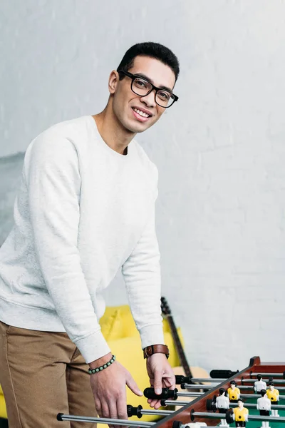 Lächelnder junger Mann mit Brille, der Tischfußball spielt und in die Kamera schaut — Stockfoto