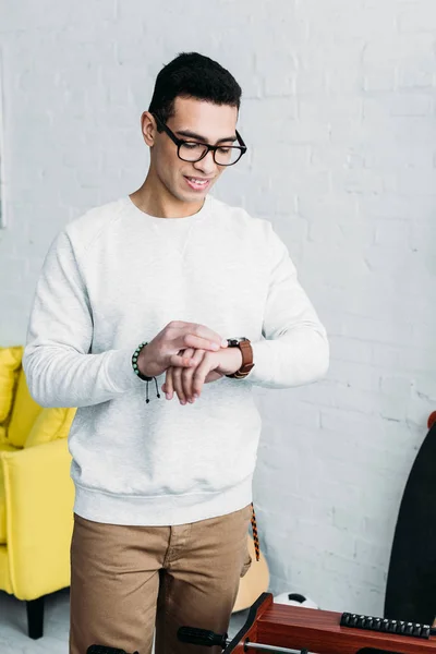 Schöner gemischter Rennmann in weißem Sweatshirt, der die Uhrzeit auf der Armbanduhr überprüft — Stockfoto