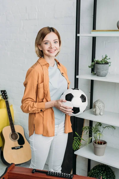 Sonriente bonita chica en naranja camisa y blanco jeans celebración de fútbol pelota - foto de stock